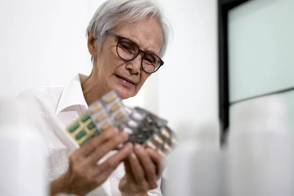アジアの高齢者の女性は 治療に薬をたくさん取らなければならないことについて強調され 高齢者は薬の丸薬やカプセルの顔の表情に退屈感を保持し 高齢者は病気に疲れている — ストック写真