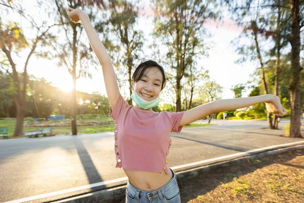 在科维德19号检疫后 科罗纳维鲁斯带着面具快乐地微笑着的亚洲小女孩 她张开绿色的胳膊站在那里 享受着呼吸新鲜空气的乐趣 — 图库照片