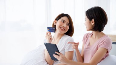 İki Asyalı kadın online alışveriş amacıyla tablet kullanıyor ve kredi kartıyla ödüyor.
