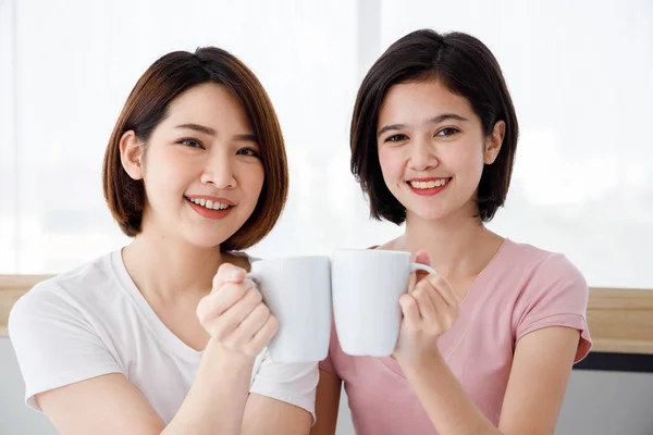 两名亚洲妇女在卧室里喝白杯中的饮料 青少年或朋友活动的概念 家庭生活方式 — 图库照片