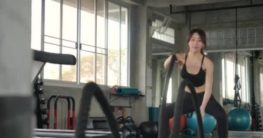 Savaş halatlarıyla spor salonunda kadın eğitimi. Güçlü, çekici Asyalı kadın ağır çekimde salonda halatlarla antrenman yapıyor..