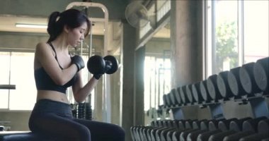 Spor salonunda kas yerine dambıl kullanan Asyalı genç bir kadının yan görünüşü. Ağır çekim. Sağlık, Egzersiz ve Spor Konsepti.
