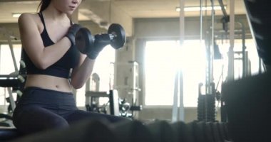 Spor salonunda kas yerine dambıl kullanan Asyalı genç bir kadının yan görünüşü. Ağır çekim. Sağlık, Egzersiz ve Spor Konsepti.