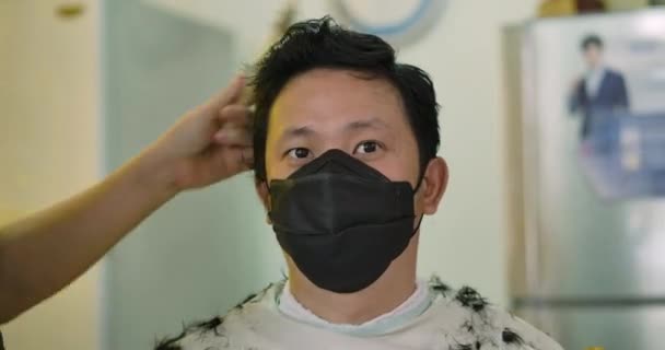 年轻迷人的男人戴着防护性医疗面罩 一边在家里理发一边看着相机 这是他的近照 留驻家中检疫大肠癌大流行预防 — 图库视频影像