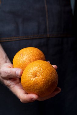 Taze ve çiğ meyve (portakal, mandalina) sunan ellerin yakın çekim. Metninizi eklemek için boşlukiçeren koyu arka plan.