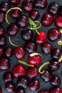 Kıymetli kırmızı ve taze vişneli biralar, dokulu ve damarlı siyah arka planda taze ve çiğ. Limon sarısı lezzet ve nane şekeri yapraklarıyla.