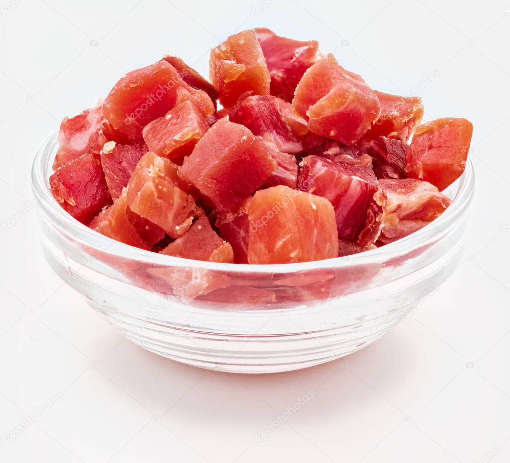 Iberian ham (serrano) cut into cubes (diced). In glass bowl. Isolated on white background.