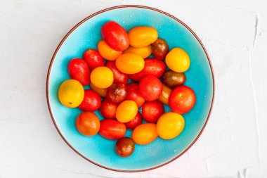 Bir kase renkli kiraz domatesleri (kırmızı, yeşil ve sarı), taze ve çiğ. Metin (kopyalama alanı) eklemek için beyaz dokulu arkaplan ve boşluk üzerine su damlaları ile. Üst Görünüm