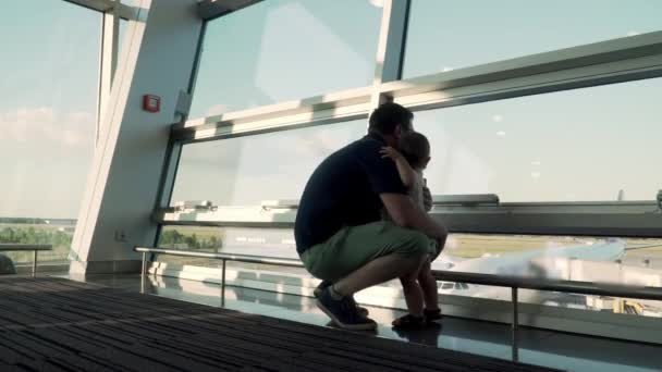 Otec a syn se dívají na letadla skrz skleněné okno. Cestování s dítětem na letišti — Stock video