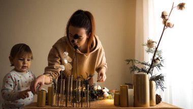 Kadın elinin köknar dallarıyla Noel çelengi yapması ve ışık tutması. Anne ve bebek.