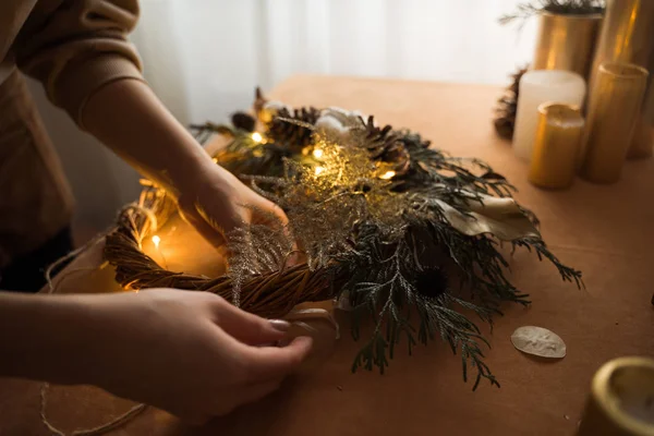 Vista superior de las manos floristas haciendo corona de Navidad con ramas de abeto y luz led. Vista superior, cero residuos —  Fotos de Stock