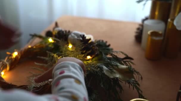 Top view női kéz, hogy karácsonyi koszorú fenyő ágak és vezetett fény. Anya a babával — Stock videók