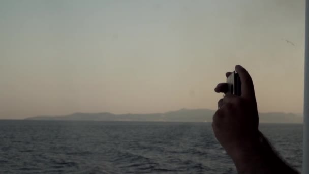 Männliche Hand fotografiert Segelboot, Meer, Sonne, Blau, Meer, Horizont und Ozean mit dem Handy. Reise — Stockvideo