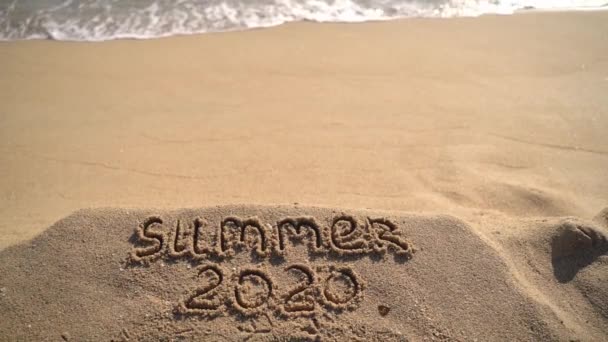 Verano 2020 texto escrito sobre arena en la playa del océano. Viaje a los trópicos y al mar — Vídeos de Stock