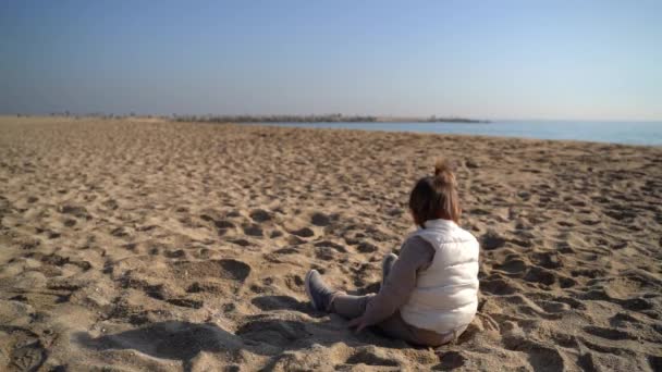 Bébé sur la plage de sable par temps froid et venteux. Assis sur la côte. Jouer avec le sable. Espagne — Video