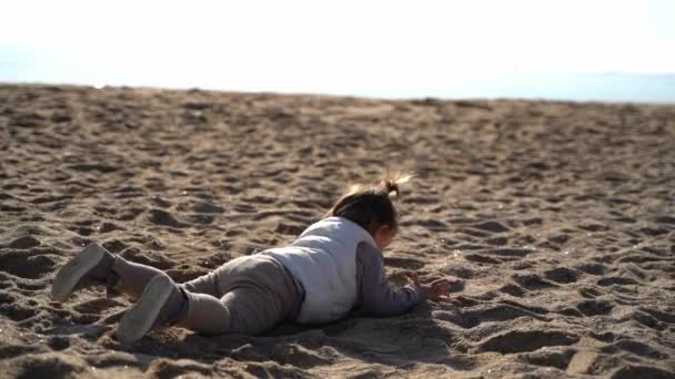 Bebé en la playa de arena en el frío día ventoso. Acostado en la costa. Jugando con arena. España — Vídeos de Stock