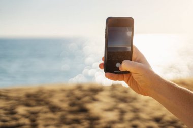 Akıllı telefonu tutan ve deniz fotoğrafı çeken bir adam. Yaz tatili fotoğrafçılığı