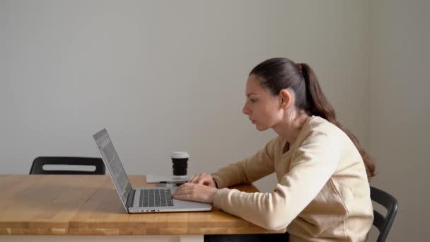 Молода жінка сидить за столом і працює на ноутбуці з поганою поставою. Проблема зі здоров'ям. Сколіоз — стокове відео
