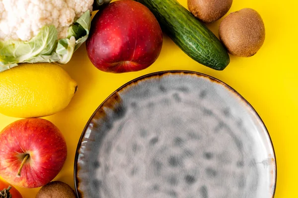 Keramische grijze lege plaat bovenaanzicht op gele achtergrond. Veel groenten en fruit. Veganistisch voedsel — Stockfoto
