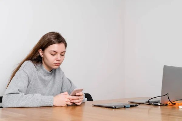 10代の少女が木製のテーブルに座り、ソーシャルメディアで挑発しています。中毒の問題 — ストック写真
