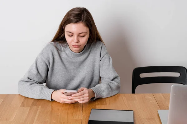 10代の少女が木製のテーブルに座り、ソーシャルメディアで挑発しています。中毒の問題 — ストック写真