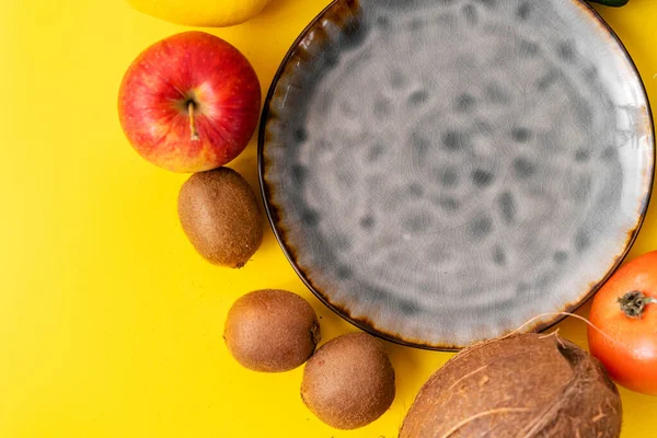 Keramikgrau leere Plattenoberseite auf gelbem Hintergrund. viel Obst und Gemüse. Veganes Essen — Stockfoto