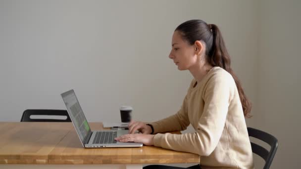 Een jonge vrouw die thuis werkt in een laptop op een houten tafel. einde van de werkdag — Stockvideo