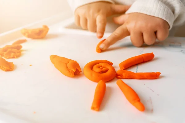 Little toddler plays play dough. Modeling orange sun. Creativity imagination