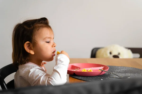 Bambina bambina mangia il suo pranzo in cucina con cucchiaio. Mani disordinate — Foto Stock
