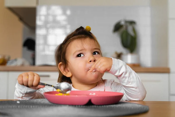 Bebê criança menina come seu almoço na cozinha com colher. Mãos sujas — Fotografia de Stock