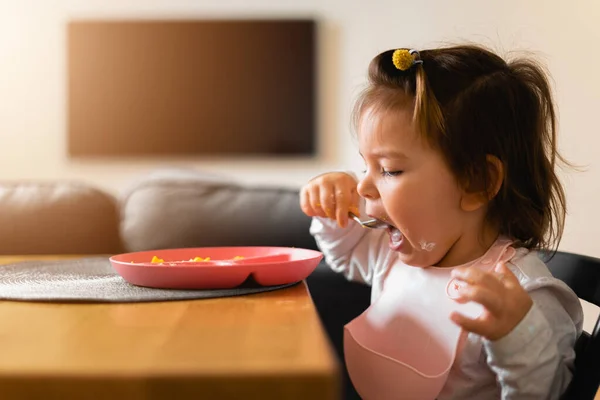 Bebê criança menina come seu almoço na cozinha com colher. Mãos sujas — Fotografia de Stock