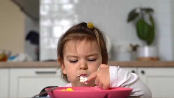 Dziewczynka je lunch łyżeczką w kuchni. Brudne ręce. — Wideo stockowe