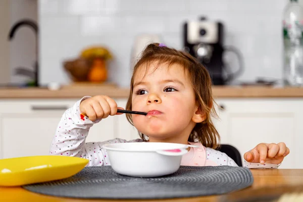 Lilla flicka äter soppa med sked i handen.. — Stockfoto