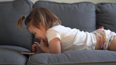 toddler sitting on the couch and playing games on the tablet, watching cartoons. modern childhood.