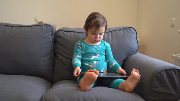 Toddler sitting on the couch and playing games on the tablet, watching cartoons. modern childhood. — Αρχείο Βίντεο