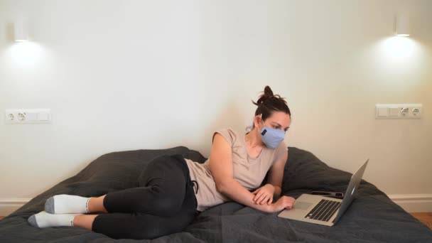 Jonge vrouw thuis op haar bed met gezichtsmasker werken op de laptop. — Stockvideo