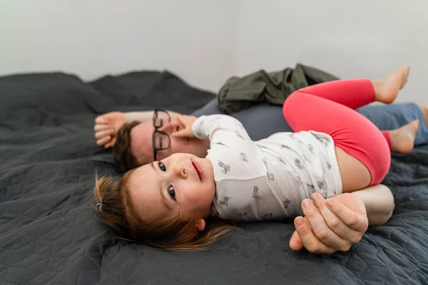 父と彼の赤ん坊の幼児の女の子はベッドの上に寝そべって午前中に抱きついていた。絆の時間を — ストック写真
