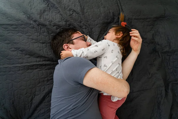 Vater und sein kleines Mädchen liegen morgens auf dem Bett und umarmen sich. Gemeinsame Zeit — Stockfoto
