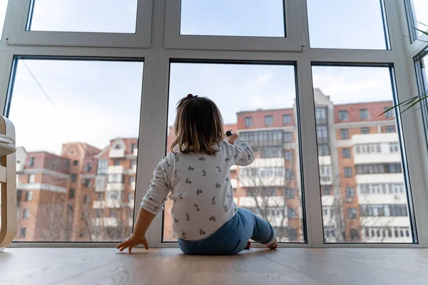 Baby toddler girl standing near the window and watching outside. Indoor play