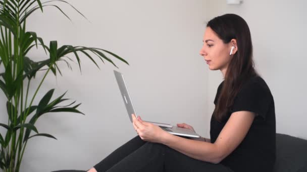 Young woman sitting at home with laptop and wireless earphones and has a video chat. Online education — Stock Video