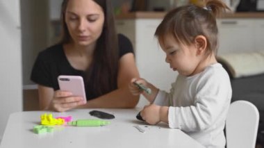 Küçük bir bebekle ev telefonunda çalışan genç bir anne anneye yakın oynuyor. Merkez, Covid-19 karantinası.