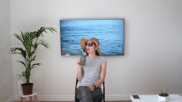 Жінка вдома прикидається на пляжі. Телевізор екран. 2020 літні карантинні подорожі. Залишайтеся вдома — стокове відео
