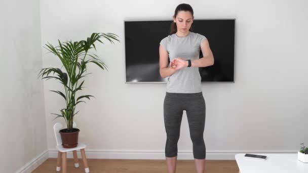 Egy fiatal nő otthon edz okos órával és telefonnal. TV képernyő. Karantén 2020 — Stock videók