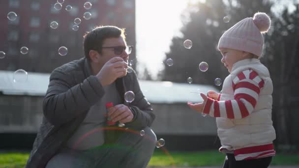 Кавказький чоловік з дитиною видував мильні бульбашки на вулиці. Повільніше. Вихідна діяльність з малюком на задньому дворі. — стокове відео