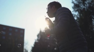 Genç beyaz adam dışarıda sabun köpüğü üflüyor. Çocuksu Mutluluk kavramı. 