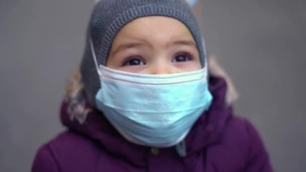 Маленький ребенок носит медицинскую маску на улице в холодную погоду. Пандемия загрязнения воздуха pm2.5 или covid-19 — стоковое видео