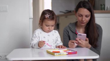 Küçük bir bebekle ev telefonunda çalışan genç bir anne anneye yakın oynuyor. Merkez, Covid-19 karantinası.