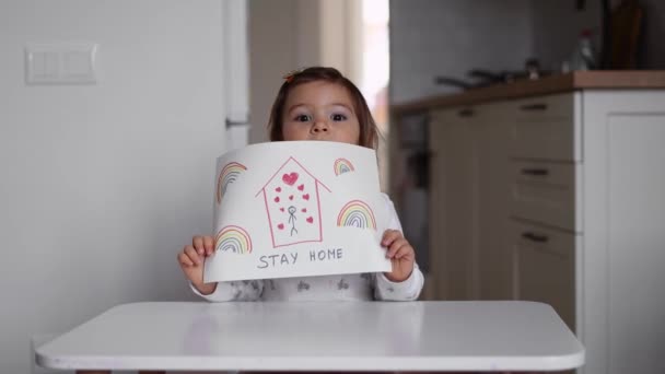 Klein meisje glimlachend met blijf thuis tekenen. Regenbogen en huis met familie. covid-19 pandemische quarantaine — Stockvideo