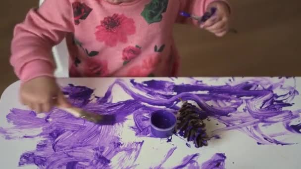 Dziewczynka maluje biały stół fioletową farbą. Kreatywny dziecięcy bałagan. Kształcenie domowe. — Wideo stockowe