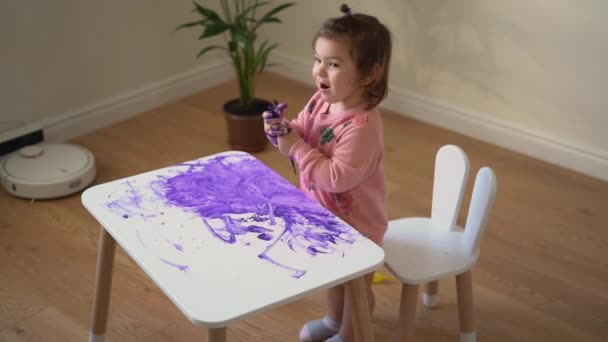 紫の塗料で白いテーブルをペイント幼児の女の子。創造的な子供の混乱。ホームスクーリング. — ストック動画